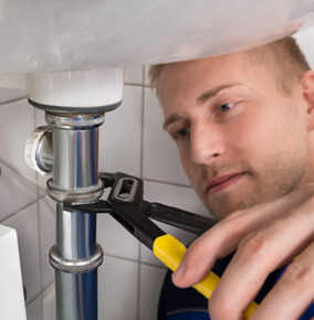 a man holding a yellow tool fixing the pipe under the bathroom sink